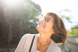 an older adults woman with glasses is outside and smiles while looking up and after learning how to cope with anxiety