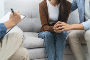 a couple sits on a couch together discussing their relationships and emotions during a therapy session