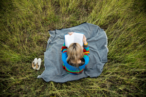 a woman sits in a grassy area on a blanket and reads about the benefits of anger management