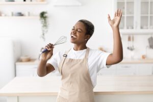 a woman in a cooking apron sings into a whisk while putting to use the information she learned in her nutrition counseling program