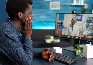a patient looks at his computer screen while participating in telehealth client services 