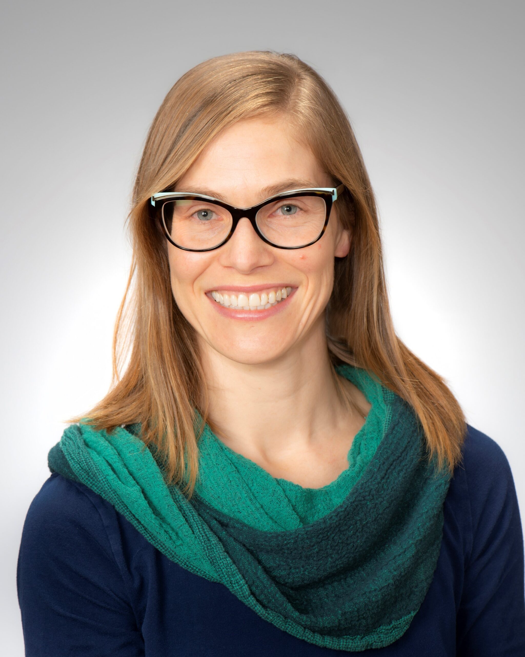 Barbara Nightingale is a smiling woman with long blonde hair. She is wearing black cat-eye glasses and a green and blue sweater.