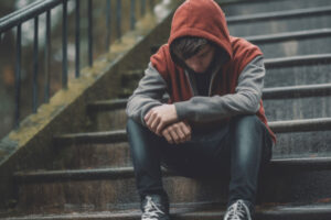 a teen boy wearing hoodie sits outside on steps thinking about where to find mental health counseling in greensburg pennsylvania