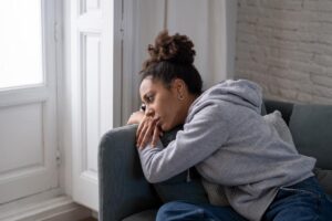 woman sits and leans on the arm of her couch thinking about the signs of emotional trauma in adults
