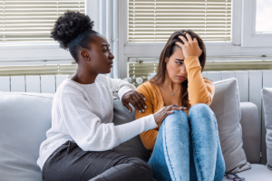 two women friends sit on a couch together has one friend consoles the other who is healing from grief
