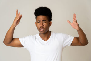 a teen boy wearing a white shirts holds up his hands while looking upset and displaying some defiant behaviors for authority
