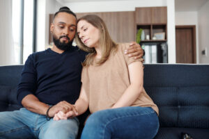 a couple sit on a couch together and hold hands while the man wonders if his wife is hiding her depression
