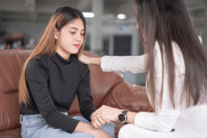 a teen girl sits on a couch in her appointment for teen counseling in fox chapel while therapist touches her shoulder