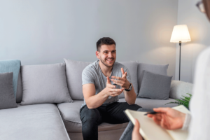 man in a grey shirt sits on a couch in his appointment for anxiety therapy in fox chapel