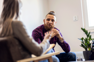 a man sits looking at his therapist while in his trauma therapy session