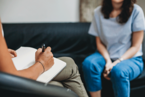 a person sits on a couch with their hands in their lap while therapist takes notes about esketamine for depression for the patient