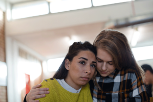 a young adults hugs another young adult while wondering how to help someone having a panic attack