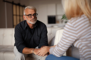 older man with glasses sits on a couch and holds hands with a woman and asks about options for mental health counseling in the fox chapel area