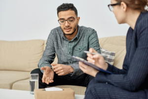 a man sits on a couch and asks a mental health professional for help finding treatment for depression in fox chapel