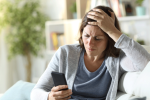 a woman appears stressed while sitting and looking at her phone and realizing the link between news and mental health