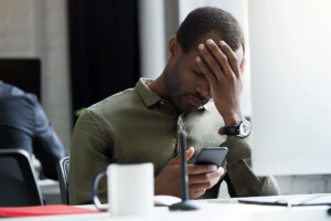 an upset man holds his phone and puts his hand to his forehead while reading tips on managing anxiety