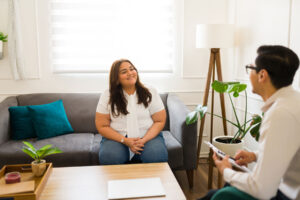 a woman sits on a couch talking to therapist who is taking notes and explaining How ADHD Treatment in Fox Chapel Can Help Your Loved One