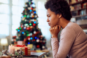 a distraught woman sits and thinks about holiday depression while a christmas tree is in the background