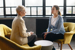 a woman sits and talks with an older woman about the importance of mental health counseling