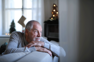 older man leans over his couch looking out the window wondering about seasonal depression