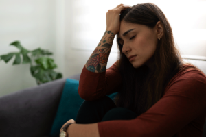 woman with prolonged grief disorde sits on a couch and holds her hand to her forehead