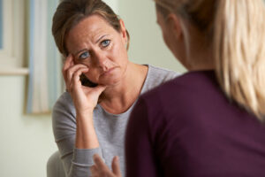 an upset woman sits with her hand on her cheek listening to a mental health professional in her schizophrenia treatment