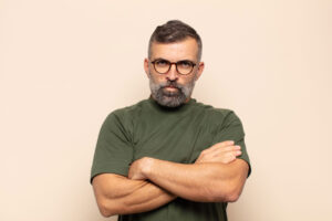 man with glasses stands with arms crossed showing signs of both depression and anger