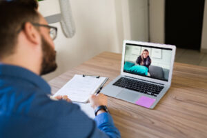 a therapist sits a desk on his laptop having a virtual therapy session with a patient