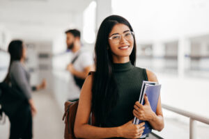 woman with glasses carries books smiling after learning more about managing anxiety in college students