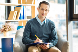 a professional with a clipboard sits in a chair discussing the differences of psychiatrist vs therapist