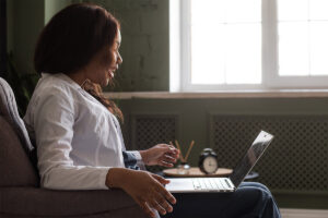 woman sits on her couch on her laptop while meeting with her therapist in online therapy