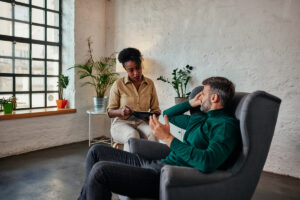 male patient sits in a chair during his ptsd treatment talking to his therapist sitting next to him