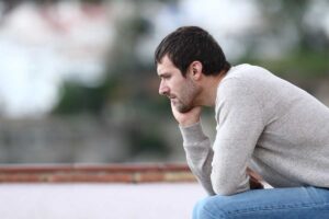 man sits outside with hand to the side of his face thinking about the signs of depression in men
