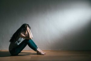 woman sits alone on the floor holding her head with her hands struggling with depression and motivation