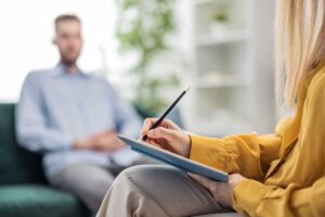 a therapist is taking notes on a notepad while discussing with a patient about bipolar II disorder symptoms