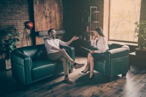 two people sit near each other on a couch and chair discussing behavioral activation therapy