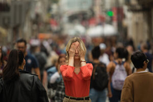 woman in a crowd covers her face with hands overcome by anxiety
