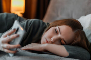 Sad woman suffering from insomnia surfing Internet or chatting using smartphone at night lying on bed. Depression Internet addiction and depression in young woman. Long web banner.